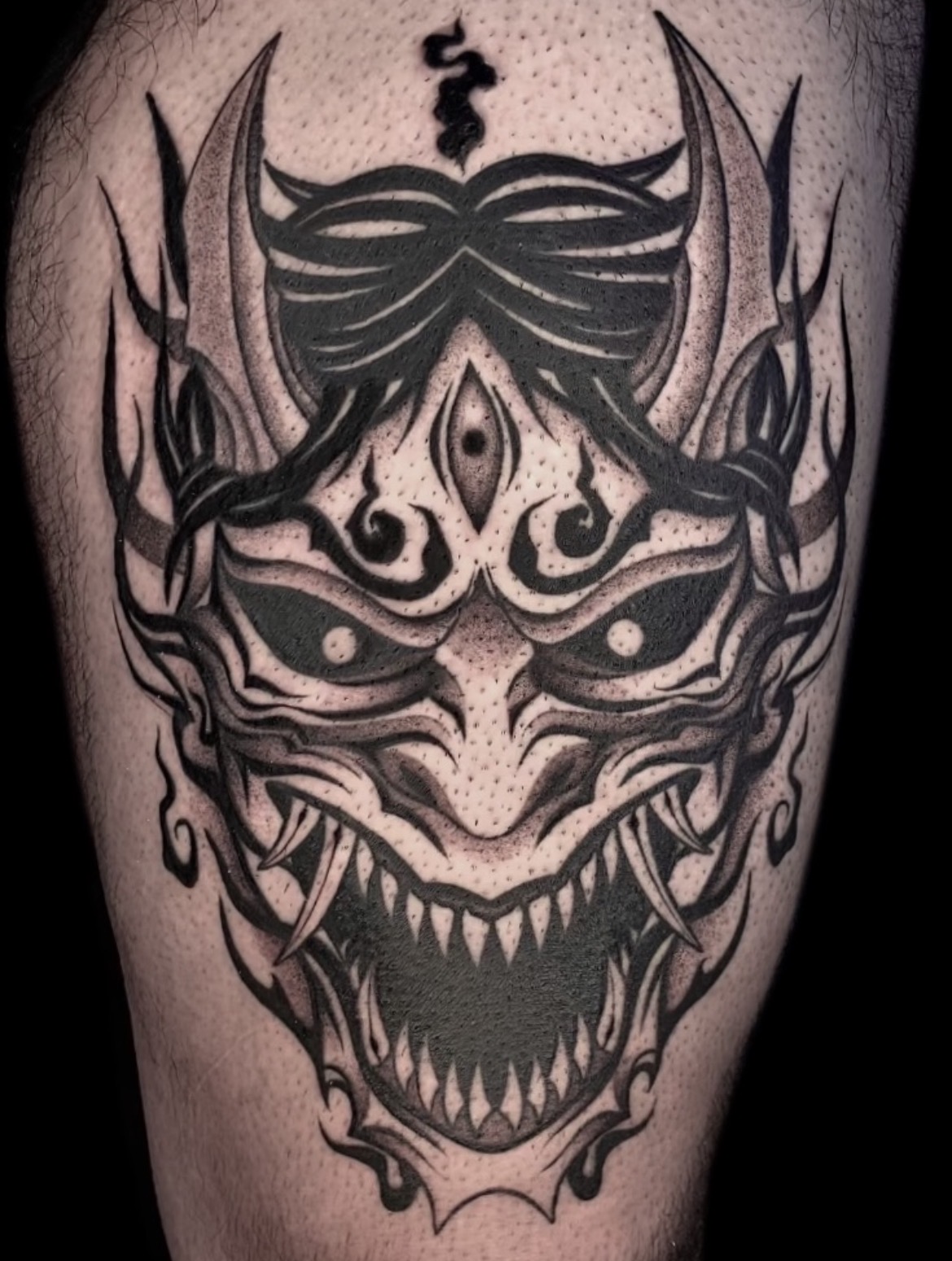 Tatuaje máscara oni tribal en muslo blackwork — CAOS Art Tattoo Chile