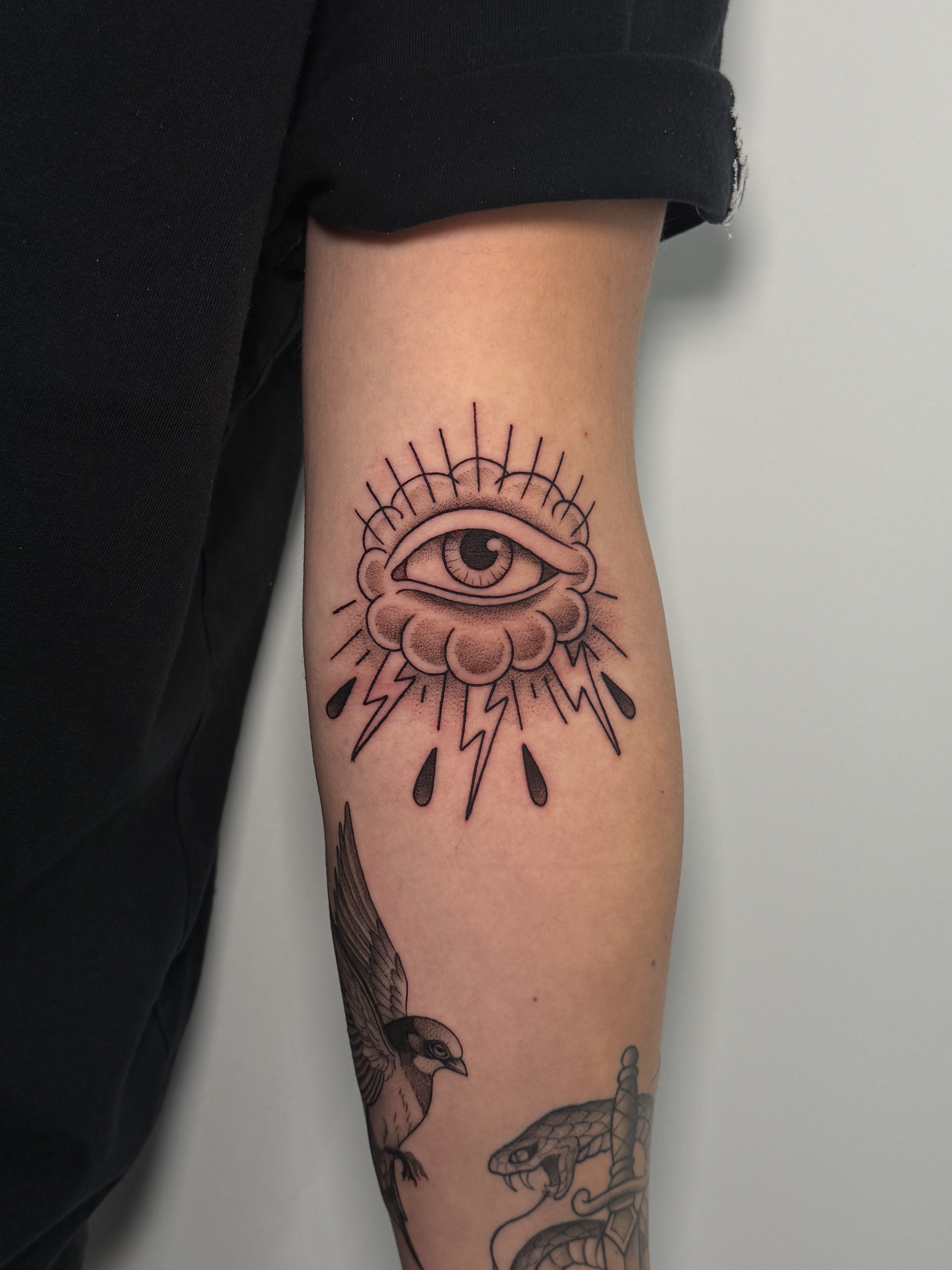Tatuaje ojo tradicional con nubes y rayos blackwork antebrazo — CAOS Art Tattoo Chile