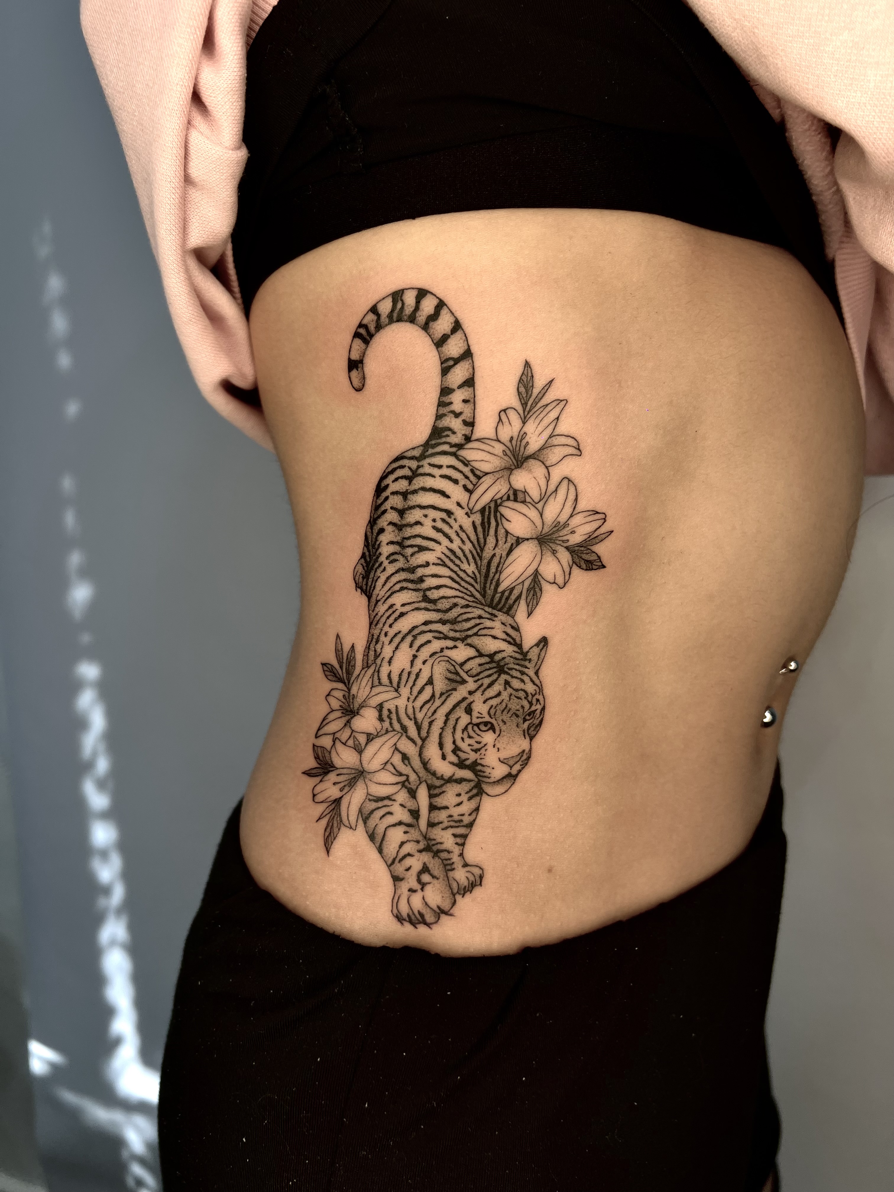 Tatuaje tigre lineal blackwork con lirios en costillar — CAOS Art Tattoo Chile