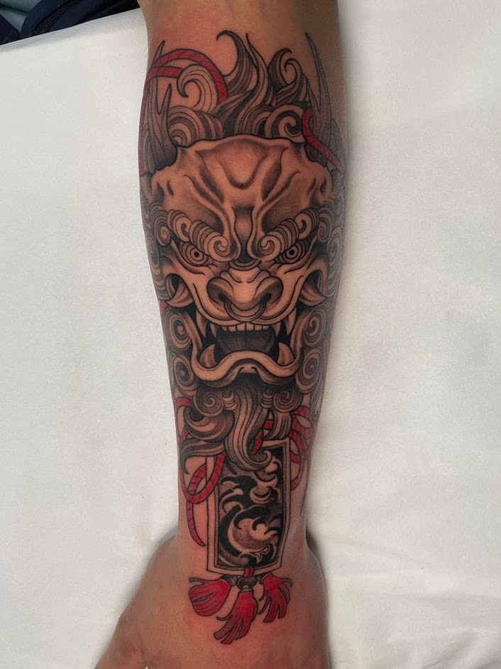 Tatuaje foo dog shisa japonés con omamori en antebrazo — CAOS Art Tattoo Chile